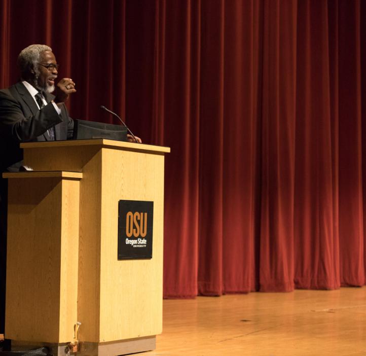 Sylvester James “Jim” Gates, Jr. spraking on stage behind podium
