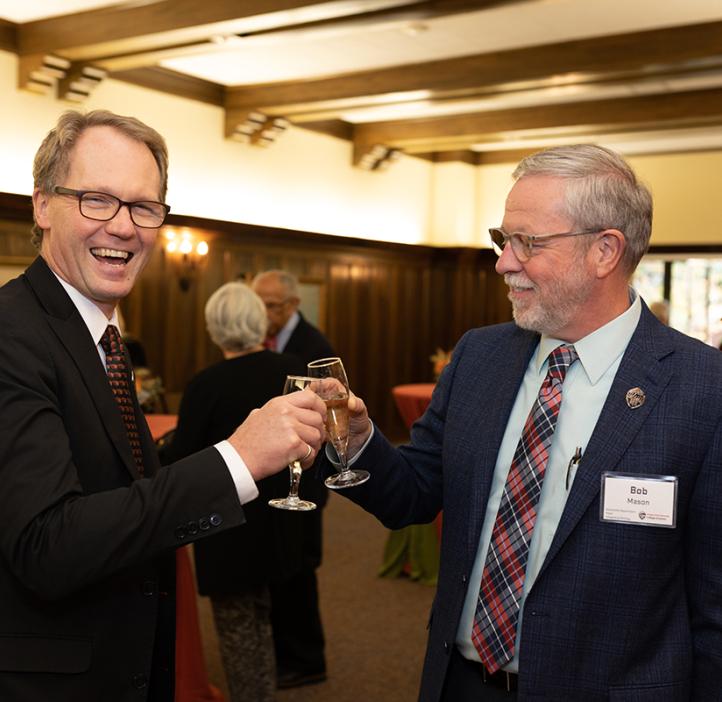 Roy Haggerty laughing and "cheers-ing" with a faculty member
