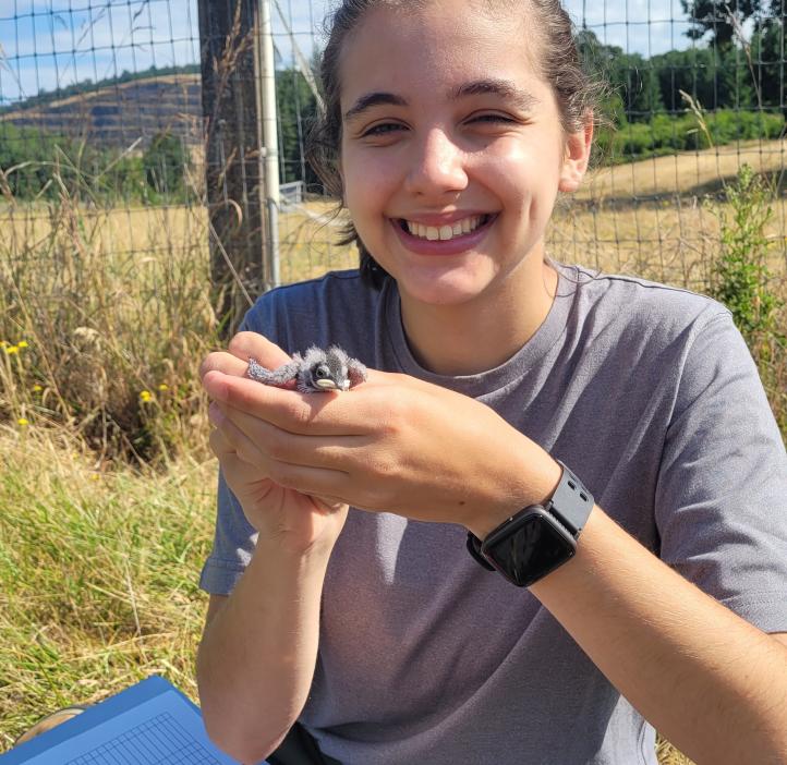 Student holding a baby bird in a field.