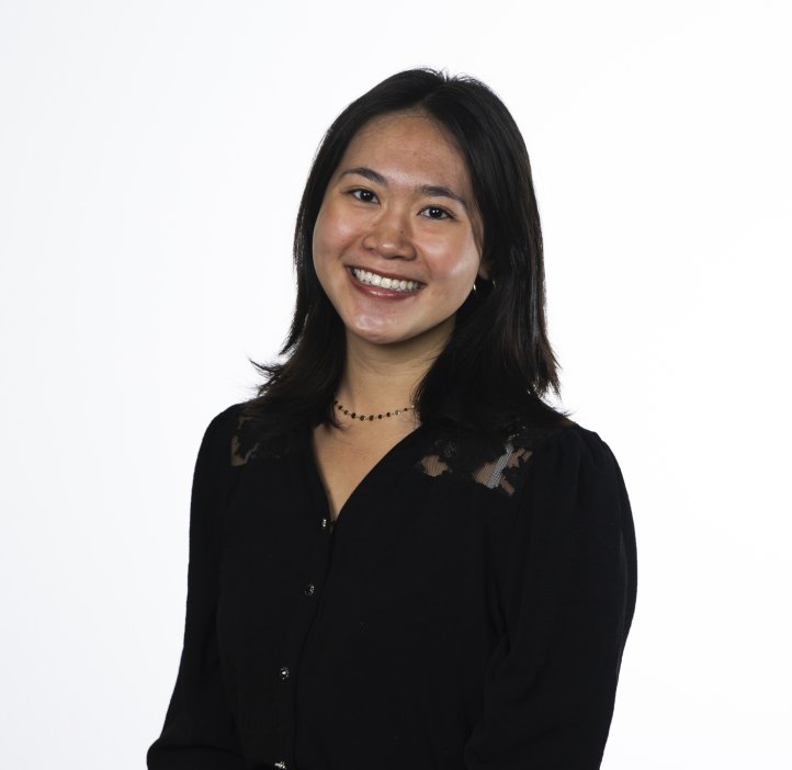 A woman in a black shirt poses for a headshot in front of a white background.