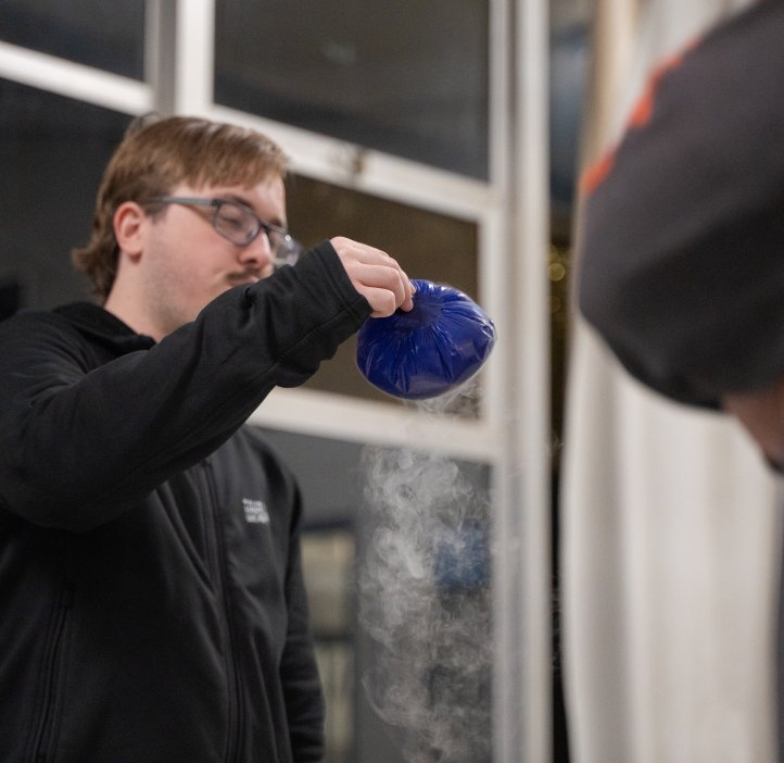 An OSU student holds up a blue bag of dry ice. The vapor is visible in the air around it. 