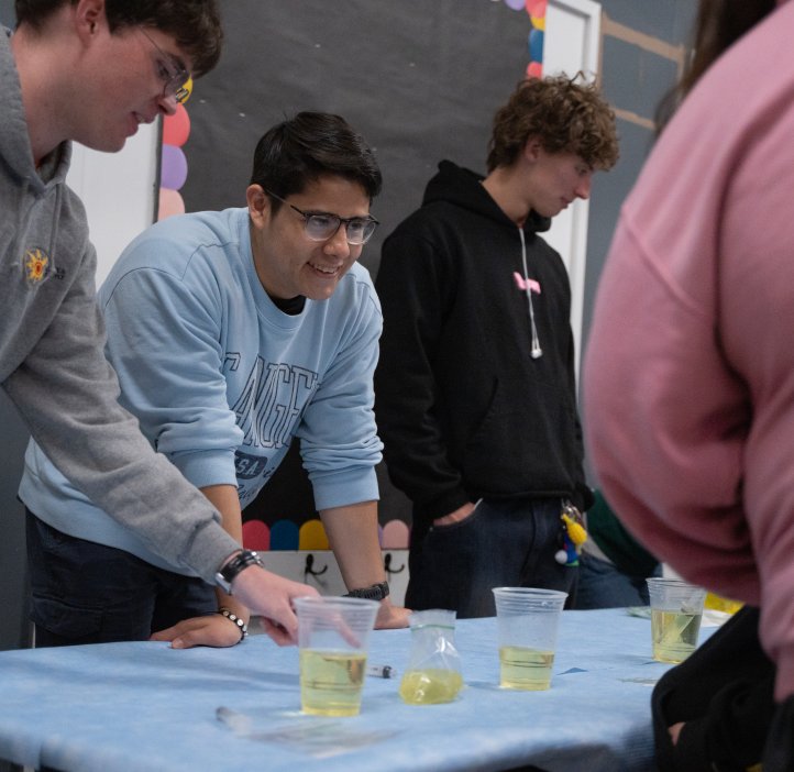 An OSU student smiles at a child across the table from him. There are containers of colorful liquid on the table between them.