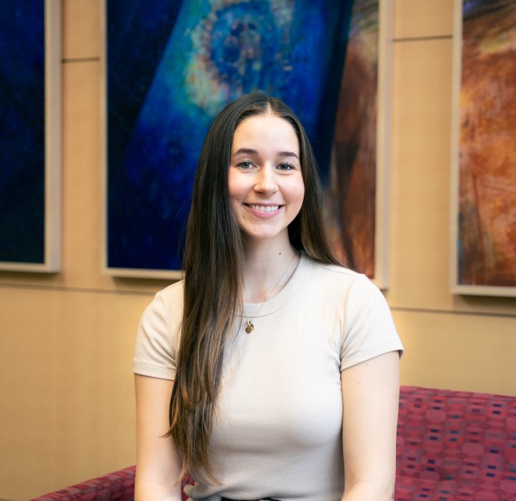 Kennedy Duff smiles for the camera in front of three colorful portraits.