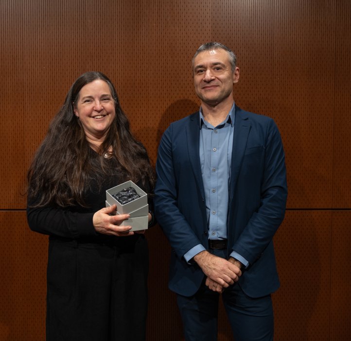 A woman in a black dress holds a glass award standing next to a man in a blue suit.