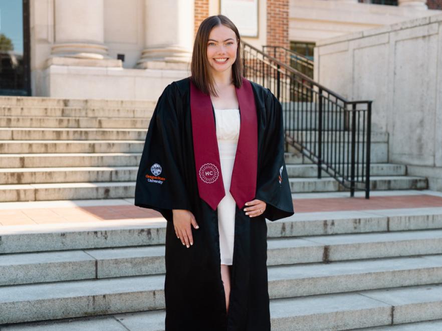 Woman standing on stairs in graduation regalia smiling